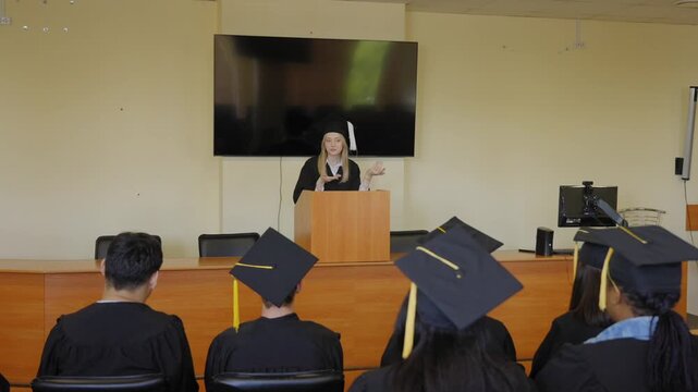 A young woman stands at the lectern and delivers a graduation speech to her classmates. 