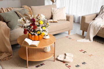 Pumpkin with autumn bouquet, book and cup of coffee on table in interior of living room