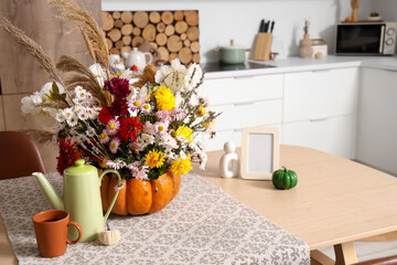 Pumpkin with autumn bouquet, teapot and mug on table in interior of kitchen, closeup