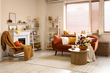 Fireplace, sofa, table and pumpkin with beautiful autumn flowers in interior of living room
