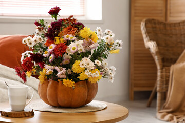 Pumpkin with beautiful autumn flowers and cup of tea on table in living room, closeup