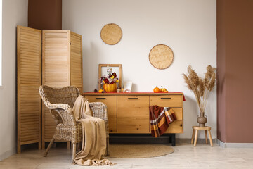 Armchair, chest of drawers and pumpkin with beautiful autumn flowers in interior of living room