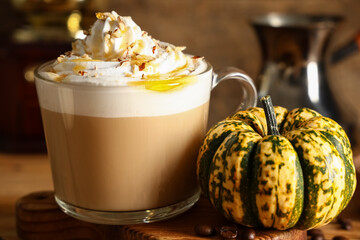 Glass cup of hot pumpkin latte with whipped cream and coffee beans on wooden background