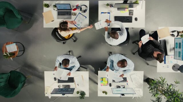 Top down view zoom in of employees collaborating on planning business strategy. Colleagues sharing market data, performance reports and insights, aligning goals and resource allocation. Camera A.