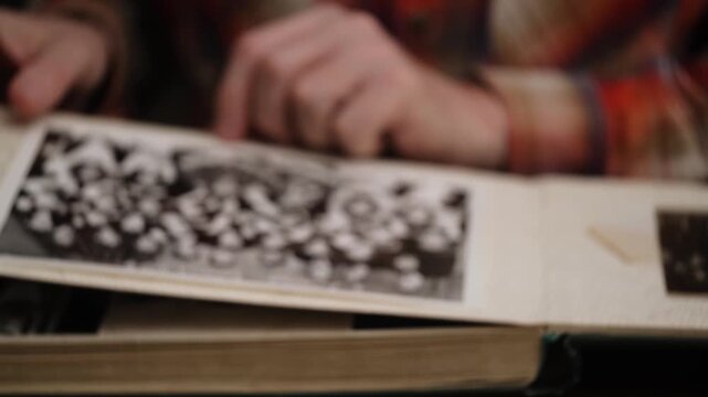 man looks at an old photo album and remembers past. flips through pages in blur black and white photographs. concept of nostalgia and memories youth. close-up. front view.