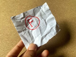 A person is holding a small, crumpled piece of paper with the failing grade 