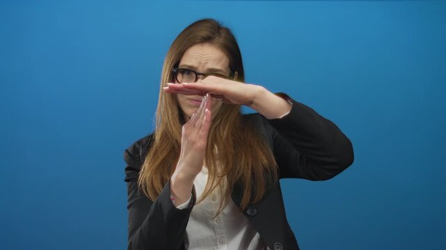 Young caucasian woman wearing glasses makes timeout gesture in blue studio setting; pause frustration.