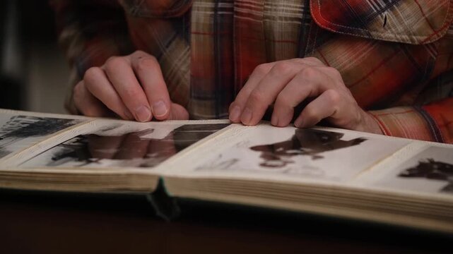 nostalgic person flipping through pages vintage family photo album, examining old black and white photographs and reliving cherished memories from past in close-up view.