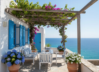 Fototapeta premium A bright Mediterranean terrace with flowers, whitewashed walls, and blue accents overlooking the clear turquoise sea on a sunny day.