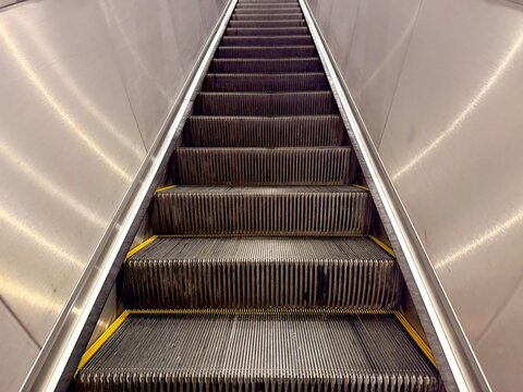A straight-on, low-angle view, moving escalator ascending upwards, emphasizing the repeating pattern steps sharp, reflective lines of the stainless steel side panels. Infrastructure transportation.