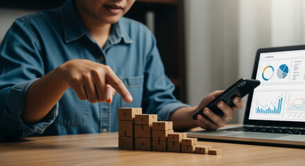 Small wooden boxes stacked in ascending order on desk representing logistic solution for e commerce growth with person using smartphone and laptop showing analytics charts
