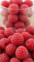 Freshly picked ripe raspberries in a glass bowl, close-up shot.