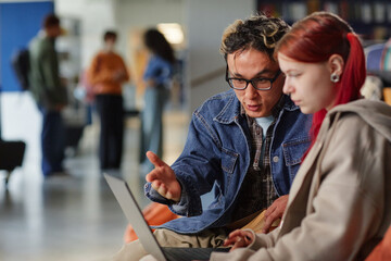 Young adult Asian man explaining something to young adult Caucasian woman using laptop in modern...