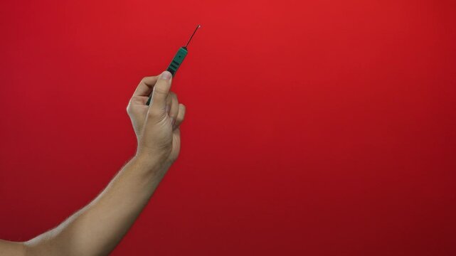Hand of a caucasian man holding a picklock tool against a vibrant red backdrop, emphasizing the isolated and secure setting.