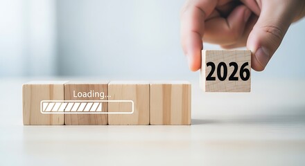 Hand placing wooden block with year 2026 on loading bar