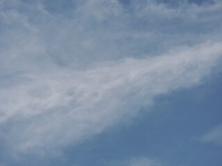 A bluish sky background with a pattern of soft white clouds. Full frame of a soft cloudy sky. Beautiful abstract blue sky and wispy clouds.