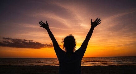 A woman with arms raised against a vibrant sunset sky.