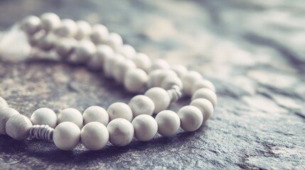 String of pale, round beads rests upon a textured, dark stone surface