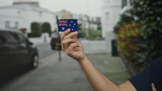 Man holding australian flag patch in an urban street, showcasing national pride and identity, with a blurred city background.