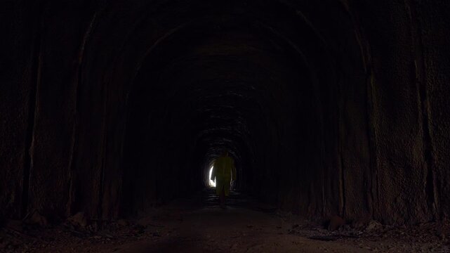 Woman in Yellow Raincoat Walks from Bright Tunnel Entrance into Deep Darkness Symbolizing Journey Through Fear and Self-Reflection Concept