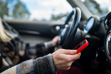 Woman driver distracted by smartphone while driving car, holding cellphone and texting, answering...