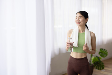 Smiling Japanese Woman in Yoga Wear Holding Water Bottle by the Window