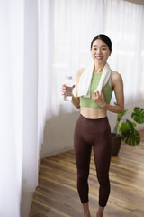 Smiling Japanese Woman in Yoga Wear Holding Water Bottle by the Window