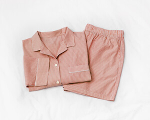 Top view of folded red striped pajama set on white bed. Minimal style, cozy, comfort pyjamas. Pink...