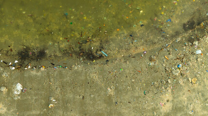 A sandy beach severely polluted with a large accumulation of plastic bottles and other trash. ocean and wave background.Environmental concept.	