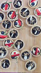 A close-up, high-angle shot of two elegant mini tarts. Each shortcrust pastry shell is filled with a rich, dark cream, likely chocolate ganache or a dark pastry cream. They are beautifully topped with
