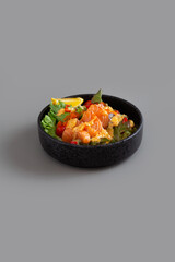 Salmon sashimi salad with green leaves, tomato and lemon on grey background.