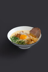 Ramen noodle in broth with Chashu pork, fresh green onions and egg yolk in bowl.