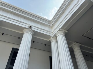upward angle shot of white, fluted neoclassical columns, corner beams, and the underside of the...