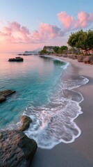 Serene Sunrise View Over a Deserted Beach with Gentle Waves Washing Ashore Reflecting Pink and Blue Sky Hues with Lush Greenery and Rocky Outcroppings