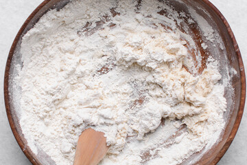 Overhead view of paratha dough being mixed in a wooden bowl, top view of flaky flatbread dough in a wood bowl, process of making paratha