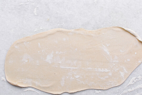 Overhead view of paratha dough being rolled out, top view of flaky flatbread dough, process of making paratha