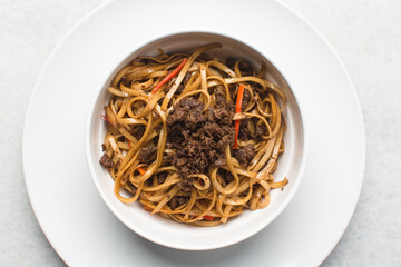 overhead view of stir-fried beef noodles in a white bowl