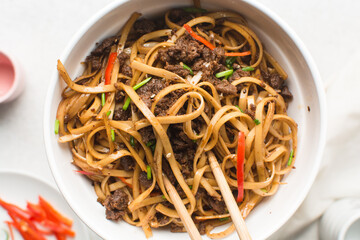 overhead view of stir-fried beef noodles in a white bowl