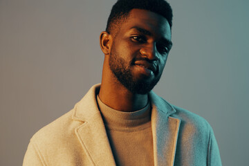 Obraz premium Stylish young man with a confident expression, wearing a light coat against a contrasting blue and beige background, showcasing contemporary fashion and personal style