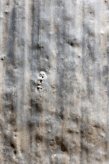 Weathered aluminum sheet displays unique texture and damage with visible holes. Outdoor industrial setting captures a grungy, rustic mood during daytime.