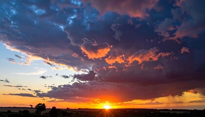 A vibrant sunset illuminates the dramatic clouds over a field