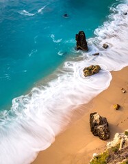 Aerial view of a sandy beach with turquoise water and rocky formations