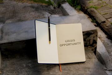 An open notebook with the financial maxim "CRISIS OPPORTUNITY" written on one page, resting outdoors on rough concrete steps.