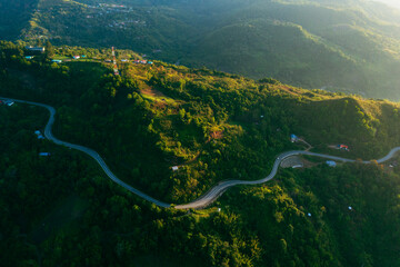 Winding mountain road leading through lush green landscape at sunrise