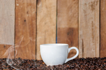 A cup of hot coffee sits on a wooden table, along with a coffee mug.