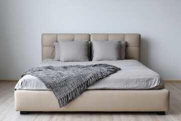 A contemporary beige upholstered bed with grey linens and throw is shown.
