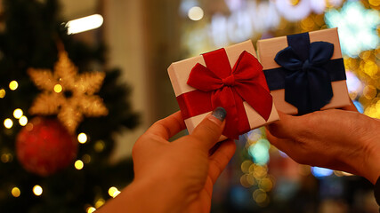 Hand of man giving gift to woman near christmas tree with bokeh background