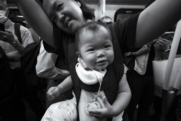 Happy baby enjoying a public commute while comfortably carried by a parent on a busy train. Urban family travel and everyday moments