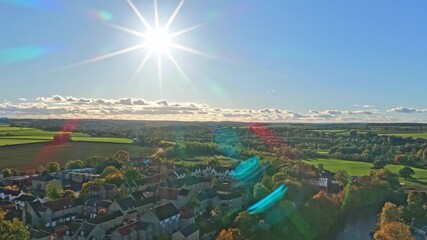 Elevated drone view unveils farmland, tree rows, open fields, residential rooftops, and sun rays dazzling above the outskirts of Wetherby, West Yorkshire, England