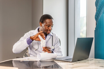 Male doctor is explaining something using an anatomical model bone while having online consultation with a patient, talking scoliosis, herniated discs, osteoporosis, diagnosing bone density issues